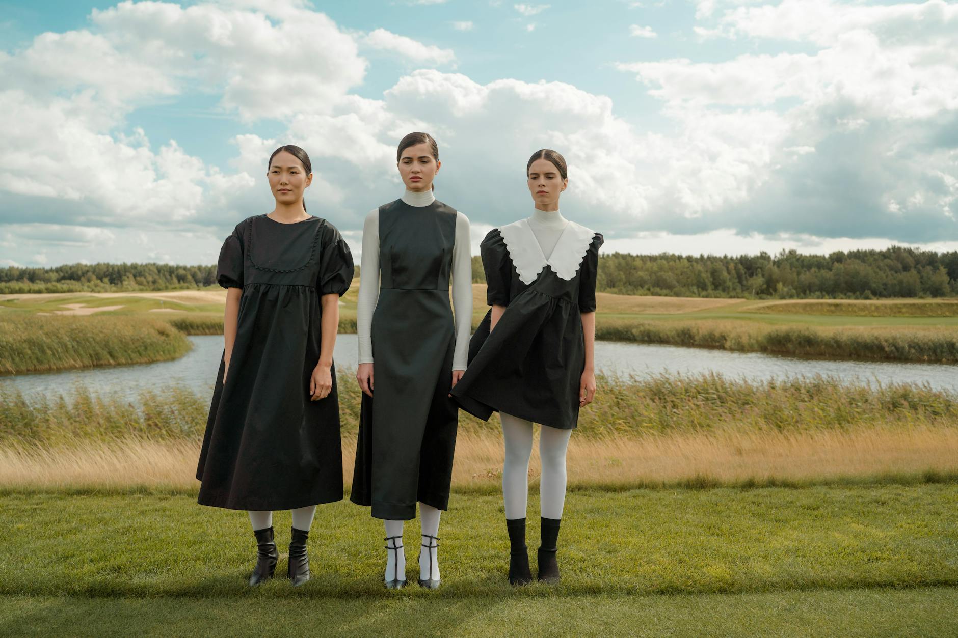 Three women in stylish black dresses standing outdoors by a lakeside