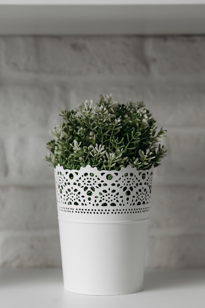who-we-are A stylish white pot with artificial green plant against a textured brick wall.