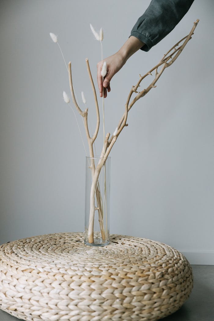 journey Stylish minimalist interior featuring a hand arranging branches in a vase on a woven table.