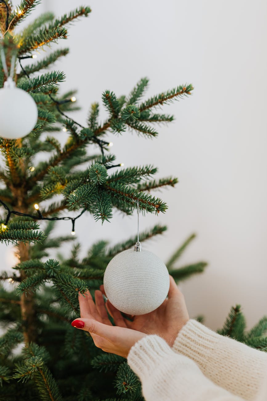 Close-up of a woman's hands decorating a Christmas tree with ornaments.