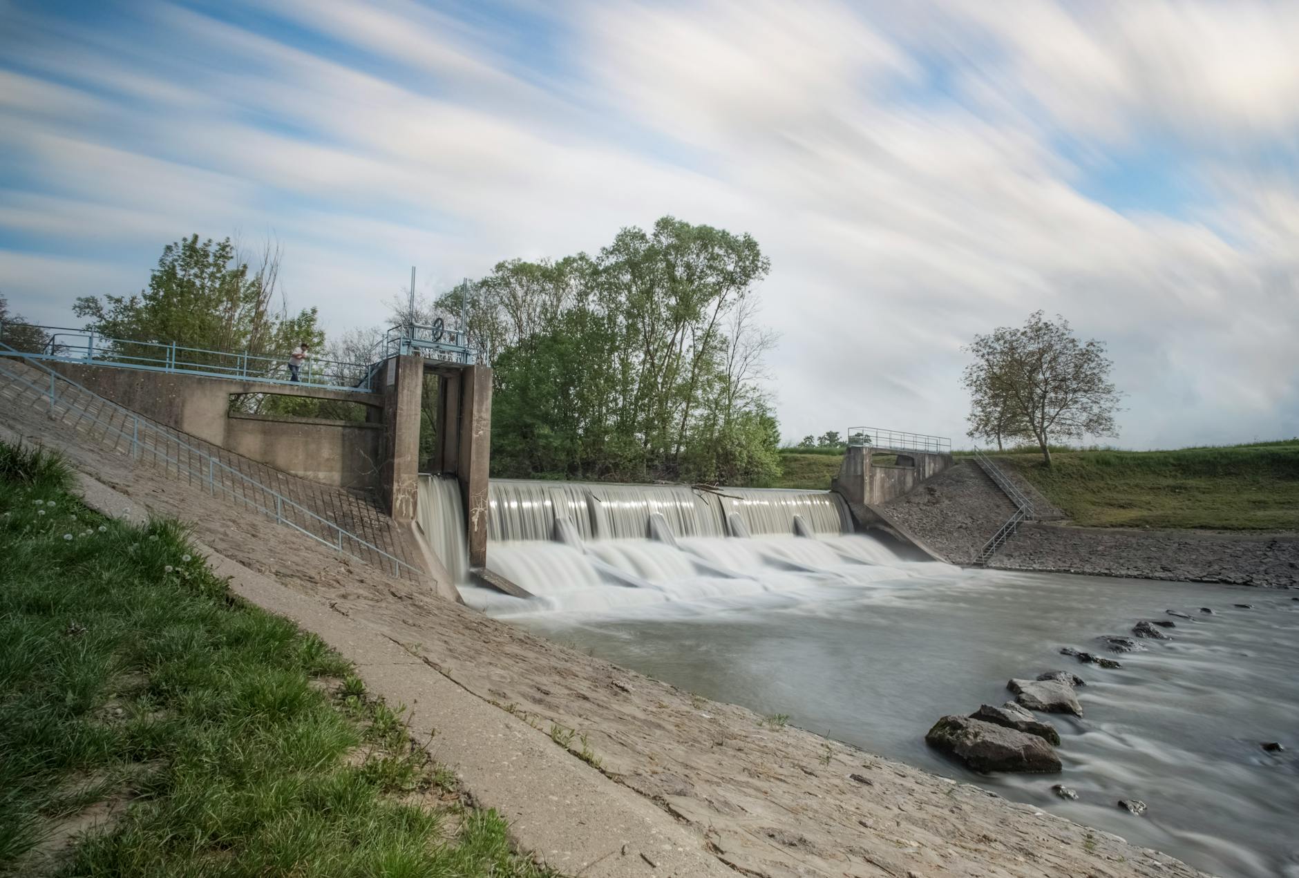 Long exposure of water flow over a dam with blurred motion and serene surroundings.