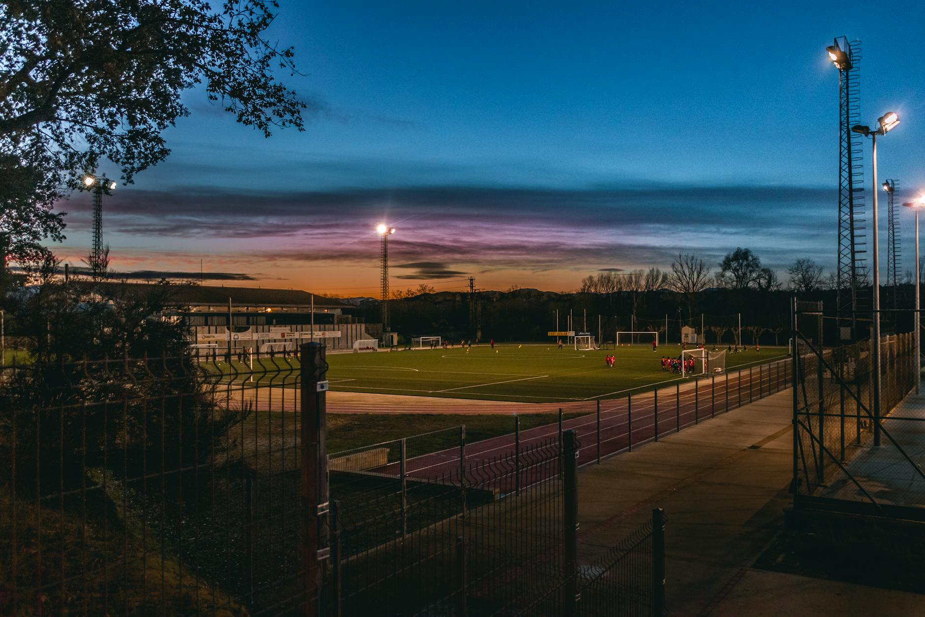 Football field illuminated by stadium lights at dusk with players practicing.