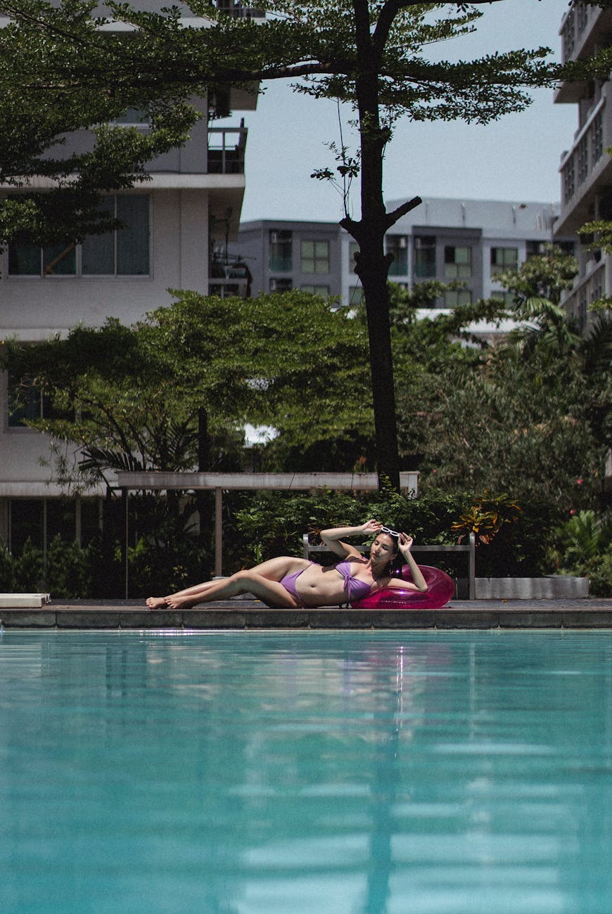 Woman lounging by a serene poolside in a tropical resort setting on a sunny day.